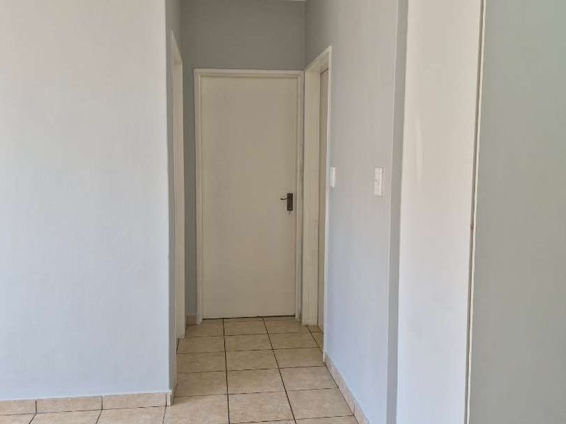 A clean, empty hallway featuring neutral grey walls, tiled flooring, and a built-in storage cupboard.