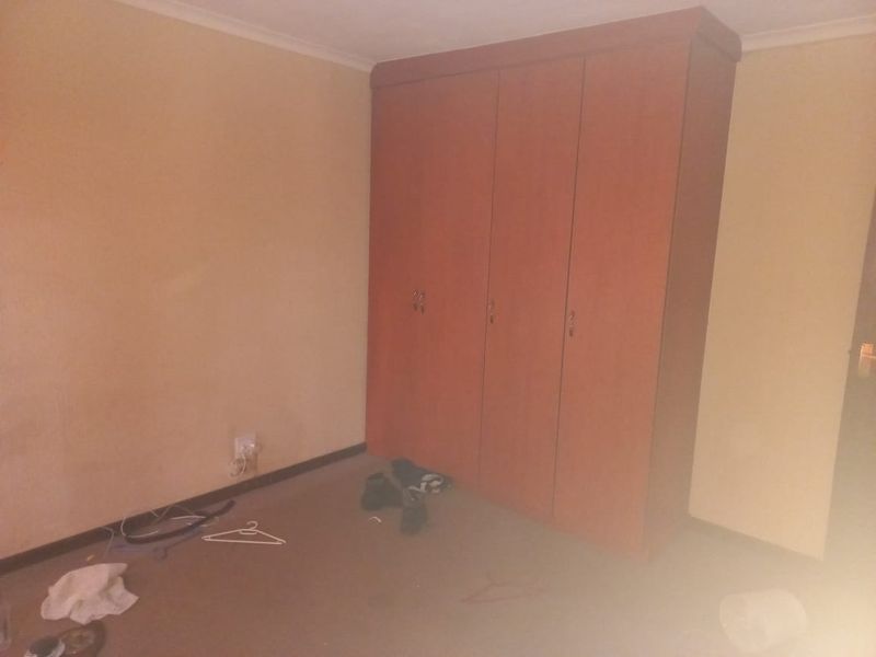 A bedroom featuring a built-in wooden wardrobe, neutral wall finishes, and carpeted flooring. The space is vacant and ready for renovation.