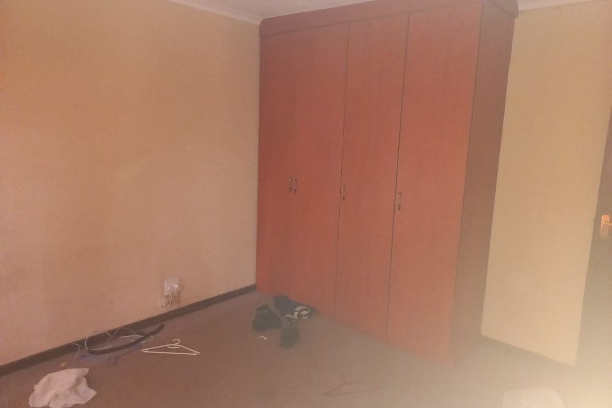 A bedroom featuring a built-in wooden wardrobe, neutral wall finishes, and carpeted flooring. The space is vacant and ready for renovation.