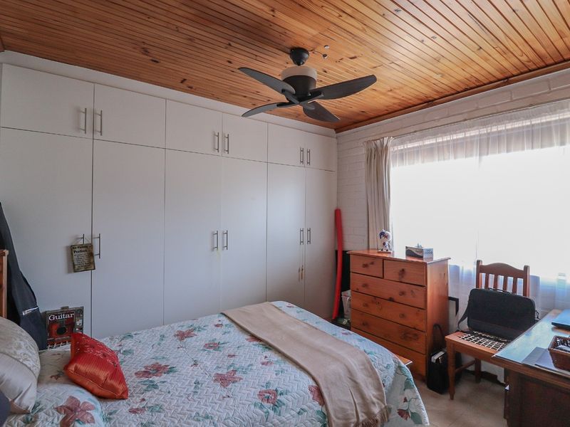 A bedroom featuring built-in cupboards, a timber-clad ceiling with a ceiling fan, and a painted brick wall.