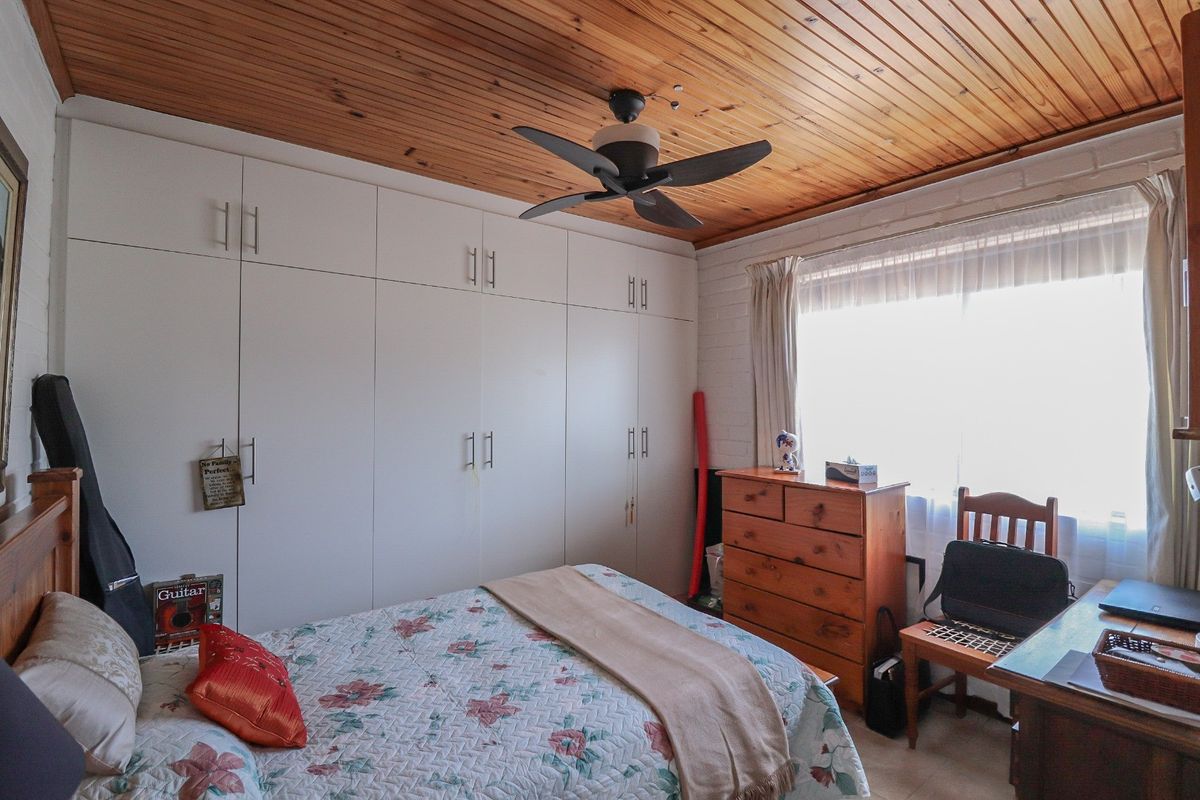 A bedroom featuring built-in cupboards, a timber-clad ceiling with a ceiling fan, and a painted brick wall.