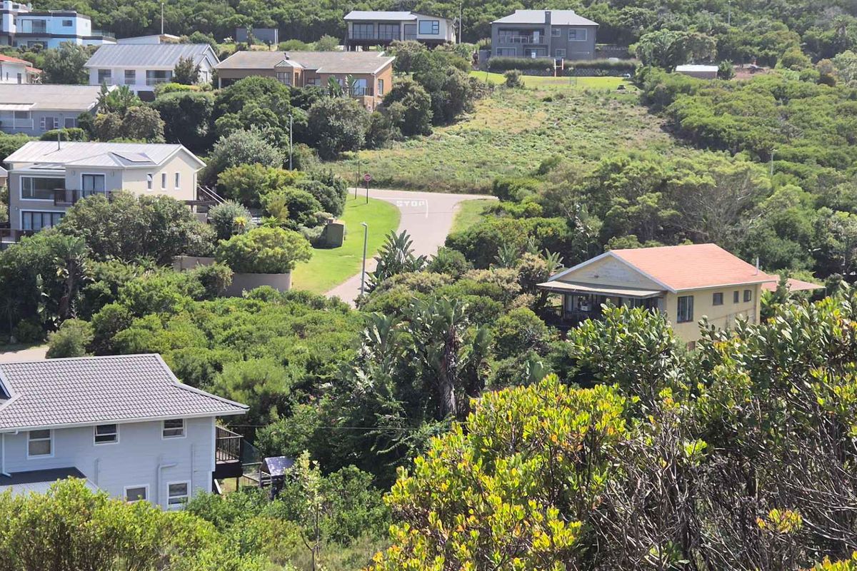 An elevated aerial view of a residential neighborhood featuring established vegetation, paved roads, and surrounding homes in a coastal or hillside setting.