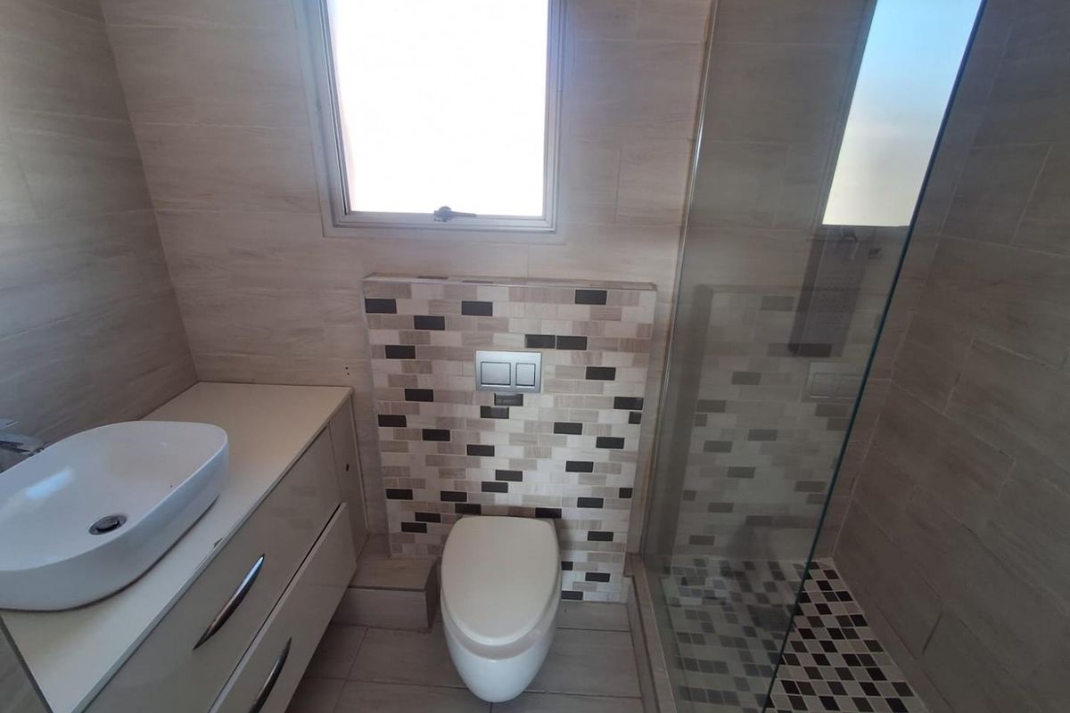 Modern bathroom featuring a wall-mounted toilet, glass-enclosed shower with mosaic tile accents, and a sleek vanity with a vessel sink.
