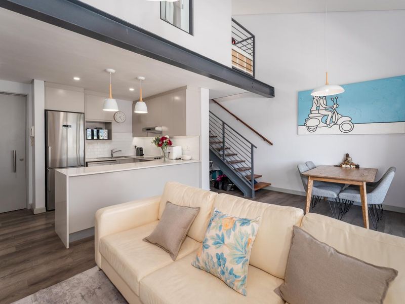 Modern open-plan apartment featuring a sleek kitchen with stone countertops, a mezzanine level, and a staircase with metal railings, finished with contemporary laminate flooring.