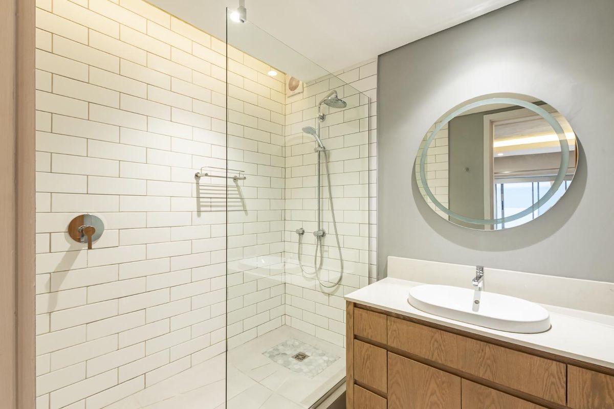 Modern bathroom featuring a glass-enclosed shower with subway tiling, a wooden vanity with a countertop basin, and a stylish backlit circular mirror.