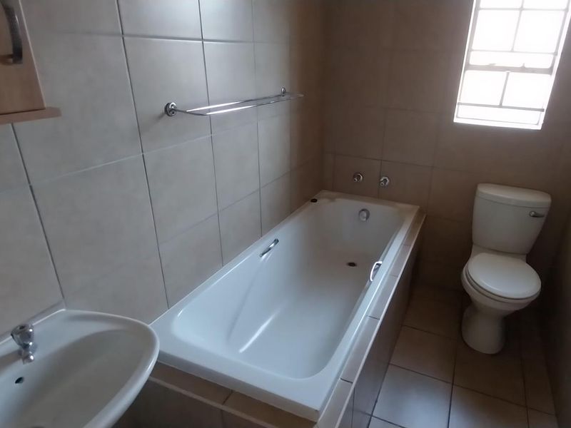 A functional bathroom featuring a built-in bathtub, pedestal washbasin, and toilet with neutral ceramic wall and floor tiling.