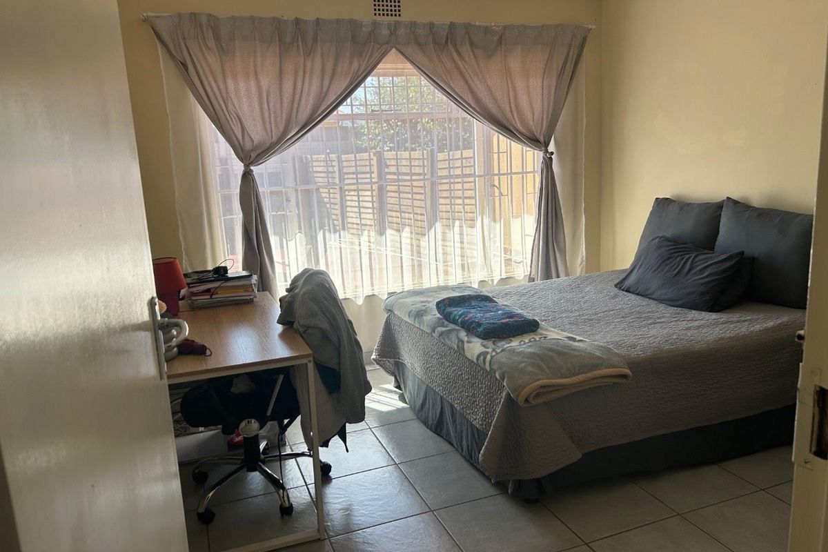 A functional bedroom featuring tiled flooring and a large window with security bars, providing natural light and a view of the exterior.