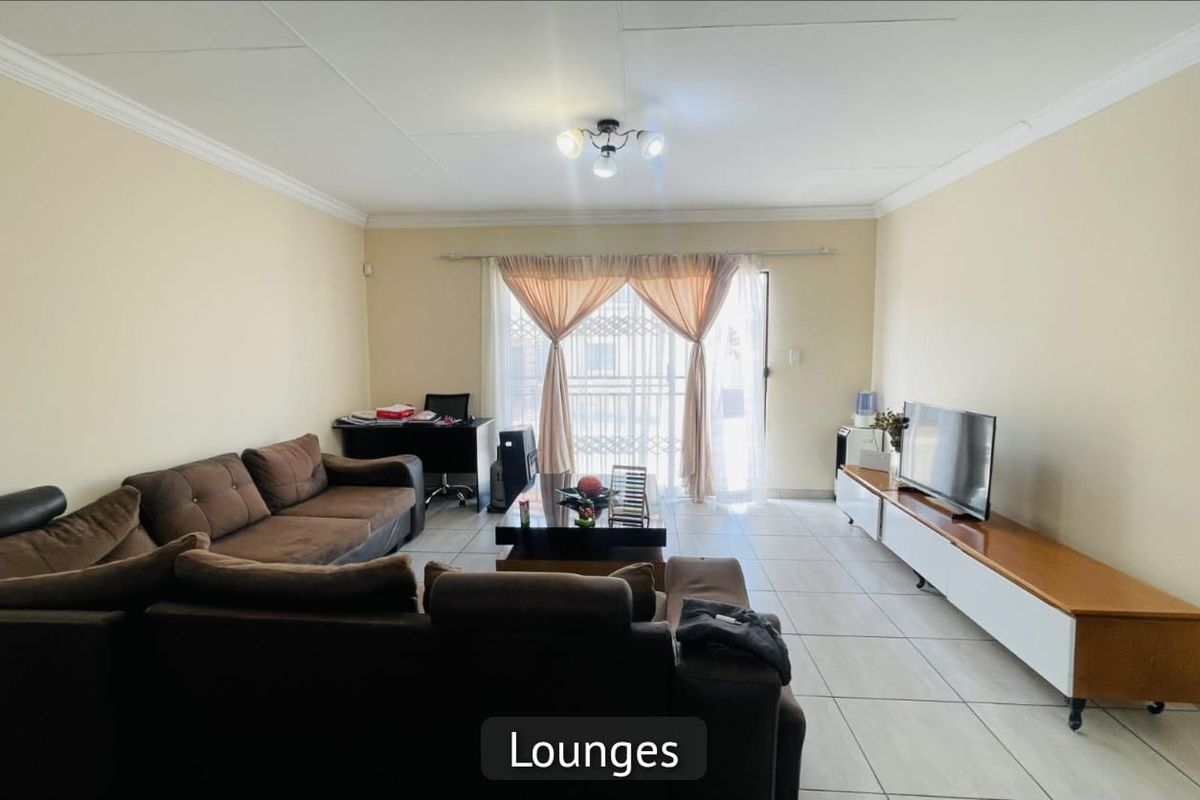 Spacious living room featuring neutral tiled flooring, crown molding, and a sliding glass door with security gate leading to the exterior.