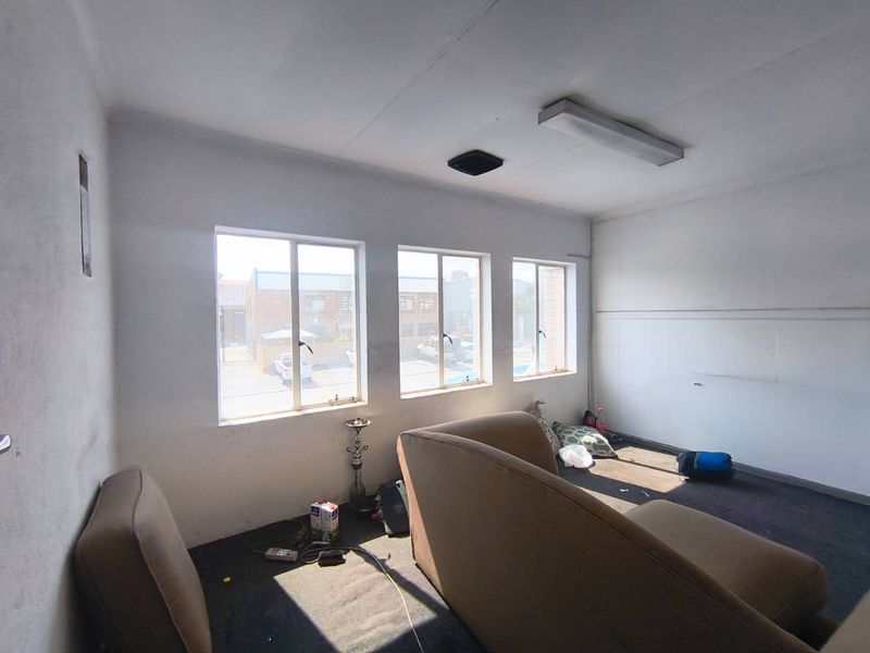 A functional office space featuring carpet flooring, aluminium frame windows, and overhead fluorescent lighting, suitable for a professional workspace or small business unit.