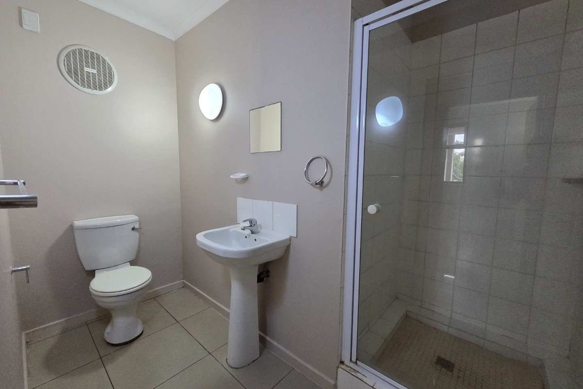 A functional bathroom featuring a pedestal sink, a white toilet, and a glass-enclosed shower with tiled walls and flooring.