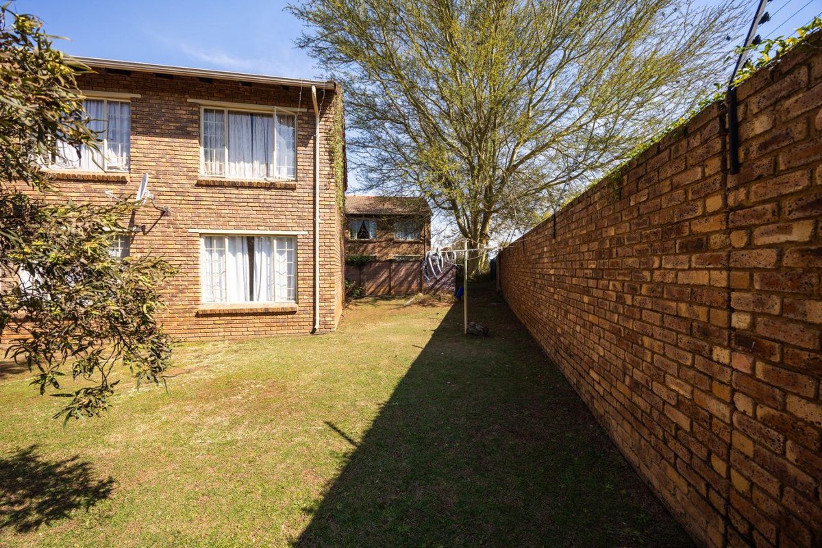 Rear view of the apartment building featuring a private lawn area enclosed by a high face brick perimeter wall with electric fencing.