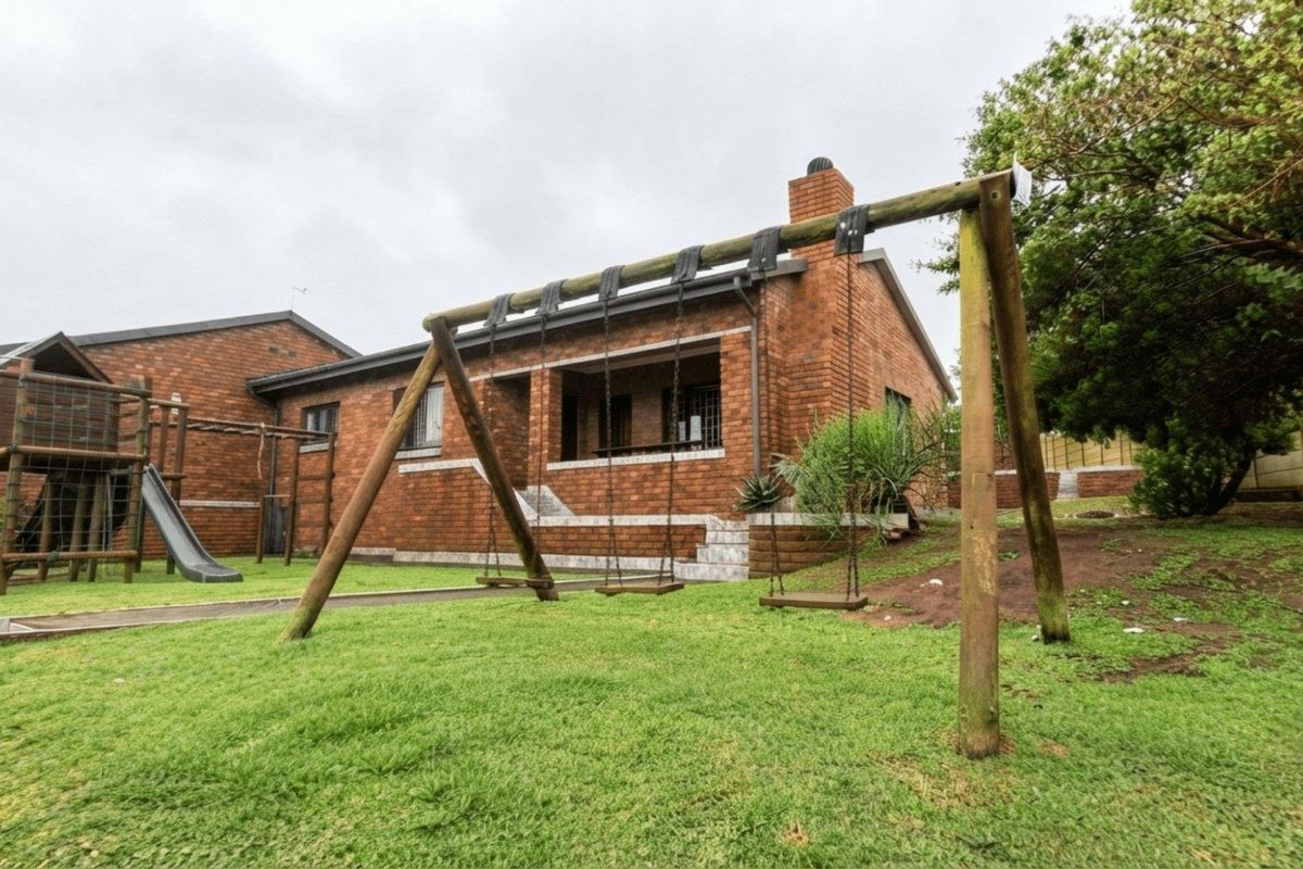 Rear view of the brick house featuring a covered patio, chimney, and a spacious garden area with lawn.