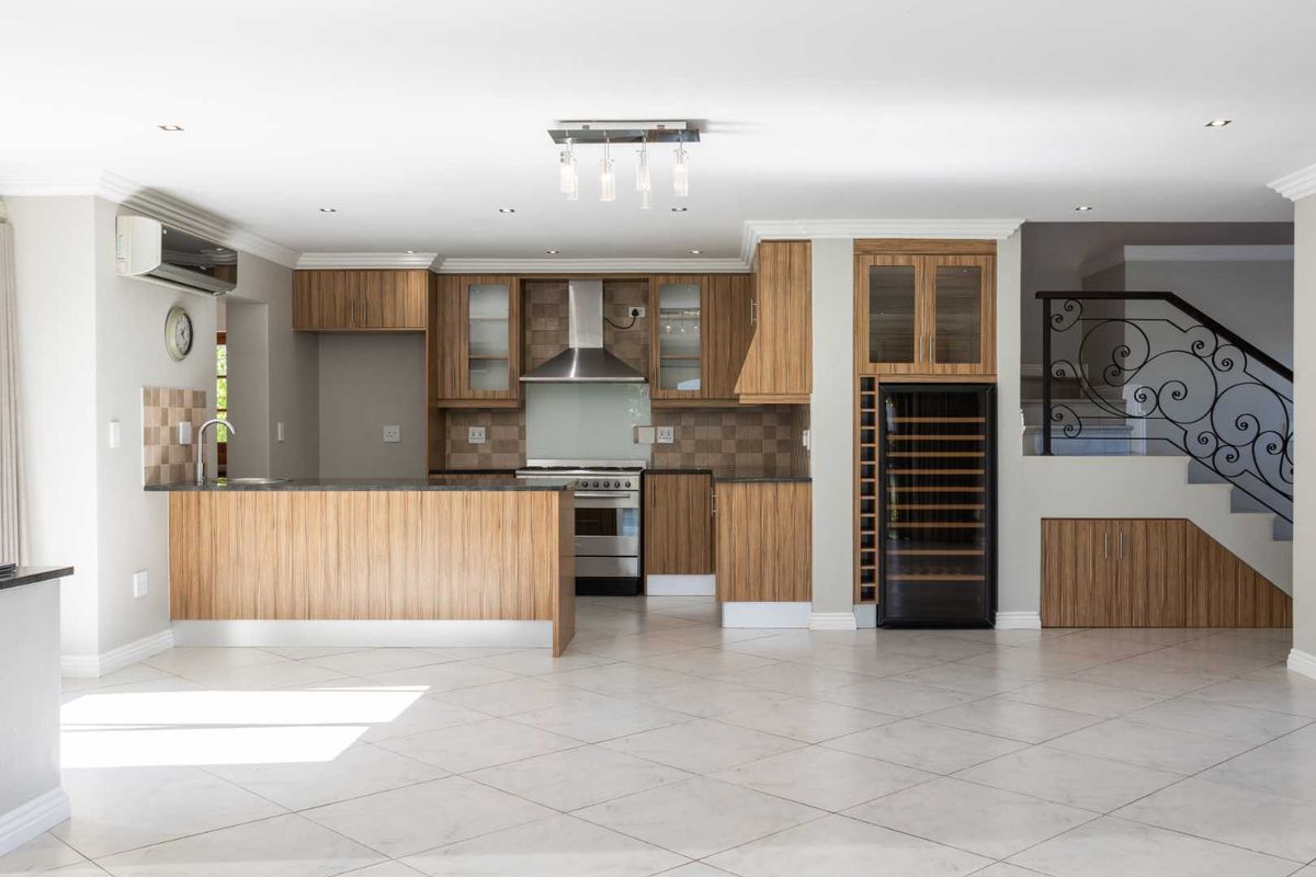 Modern open-plan kitchen featuring wood veneer cabinetry, stone countertops, integrated wine cooler, and a feature staircase with wrought iron balustrade.