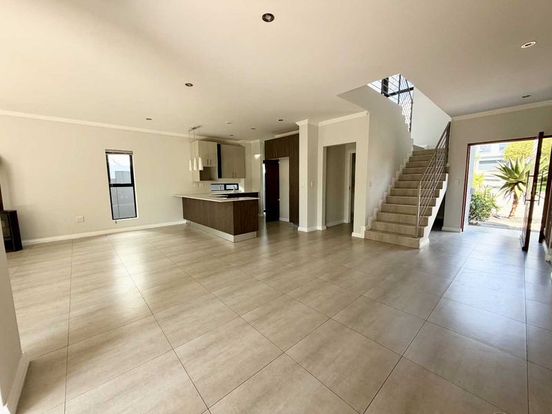 Spacious open-plan living area featuring a modern kitchen with island, tiled flooring, and a staircase leading to the upper level.