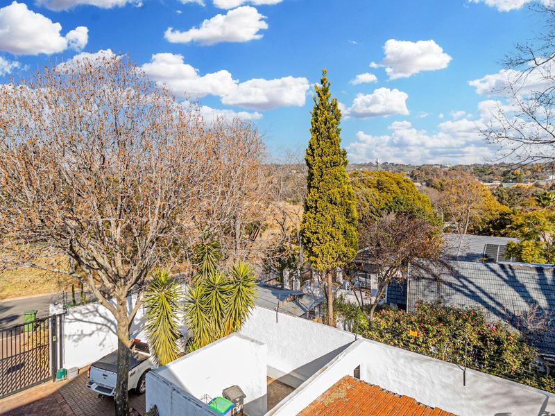 An elevated view overlooking the surrounding neighbourhood, featuring mature trees, perimeter walls, and a paved driveway entrance.