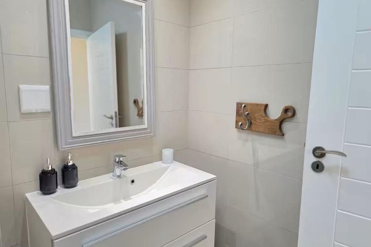 A modern bathroom featuring a sleek white vanity with integrated basin, chrome faucet, and a framed wall mirror against neutral tiled walls.