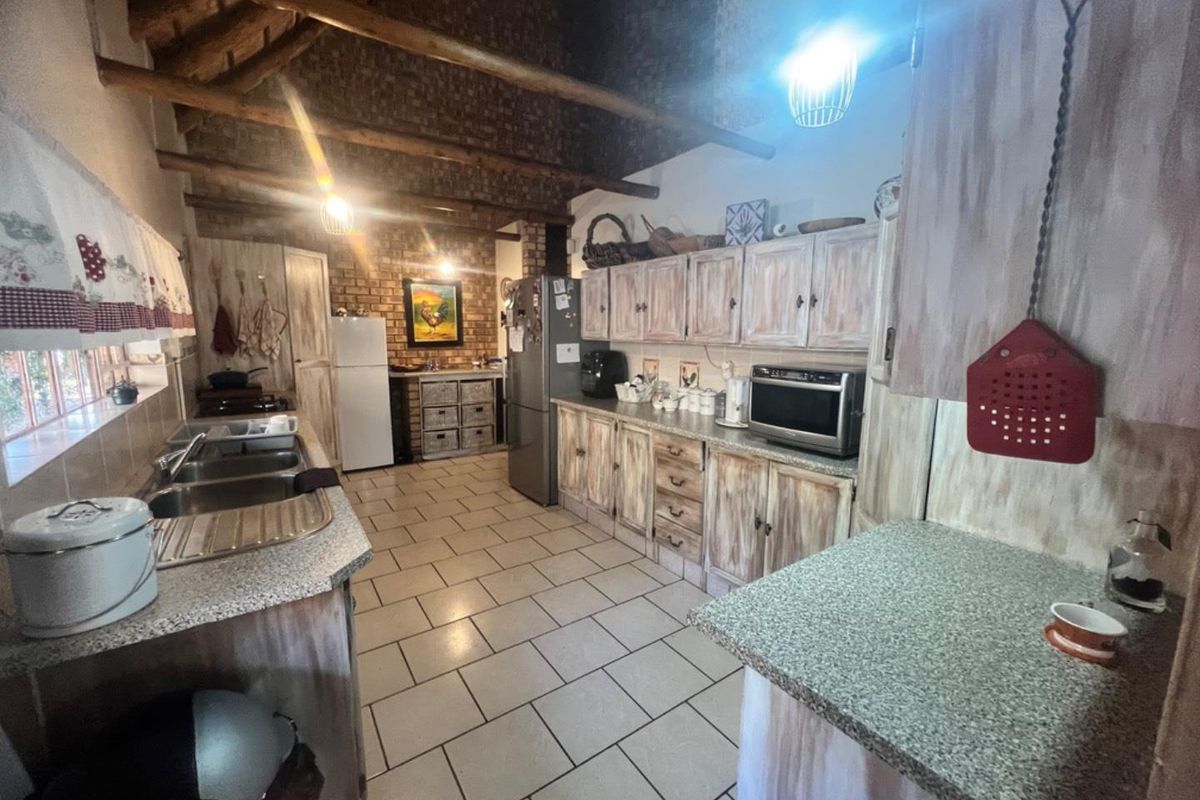 A rustic kitchen featuring exposed timber ceiling beams, brick wall accents, tiled flooring, and extensive built-in cabinetry with a distressed finish.