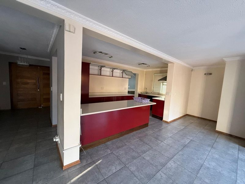 Open plan kitchen area featuring red cabinetry, stone countertops, and tiled flooring, seamlessly connected to the entrance hall.