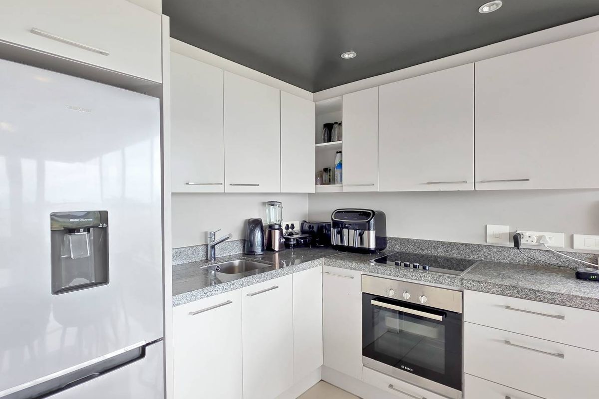Modern kitchen featuring white cabinetry, granite countertops, built-in oven, electric cooktop, and a contrasting dark ceiling finish.