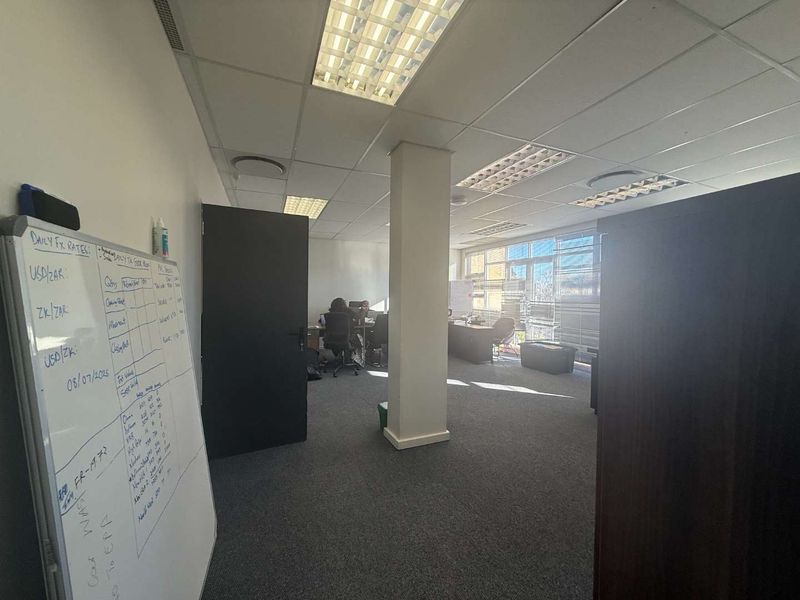 A functional open-plan office space featuring suspended ceilings, recessed lighting, carpeted flooring, and large windows providing natural light.