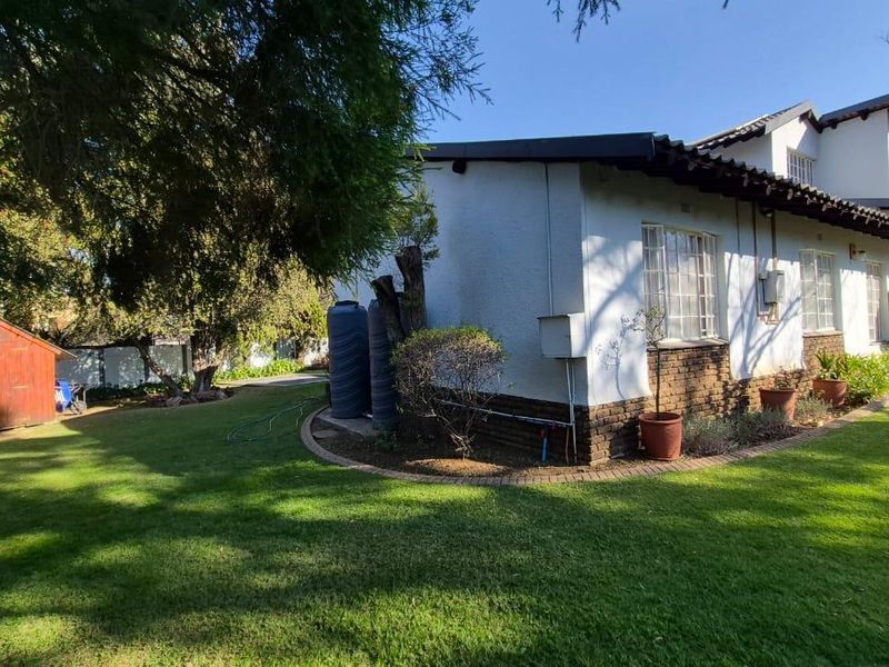 Rear view of the property featuring a well-maintained lawn, established garden, timber shed, and exterior water storage tanks.