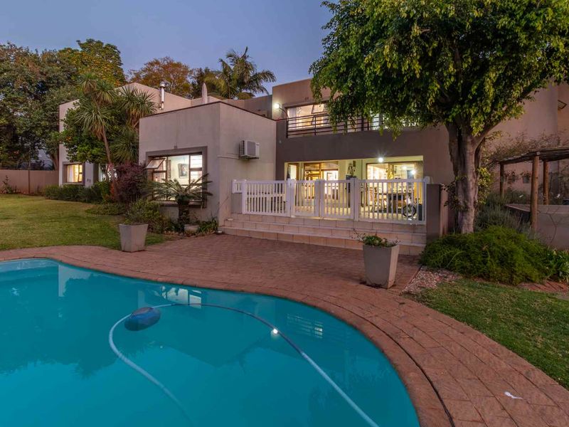 Rear view of the property featuring a swimming pool, paved deck, raised patio area, and an upper-level balcony.