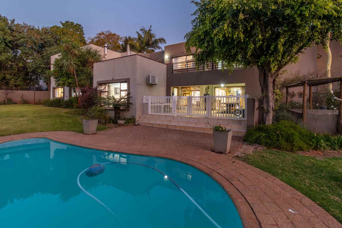 Rear view of the property featuring a swimming pool, paved deck, raised patio area, and an upper-level balcony.