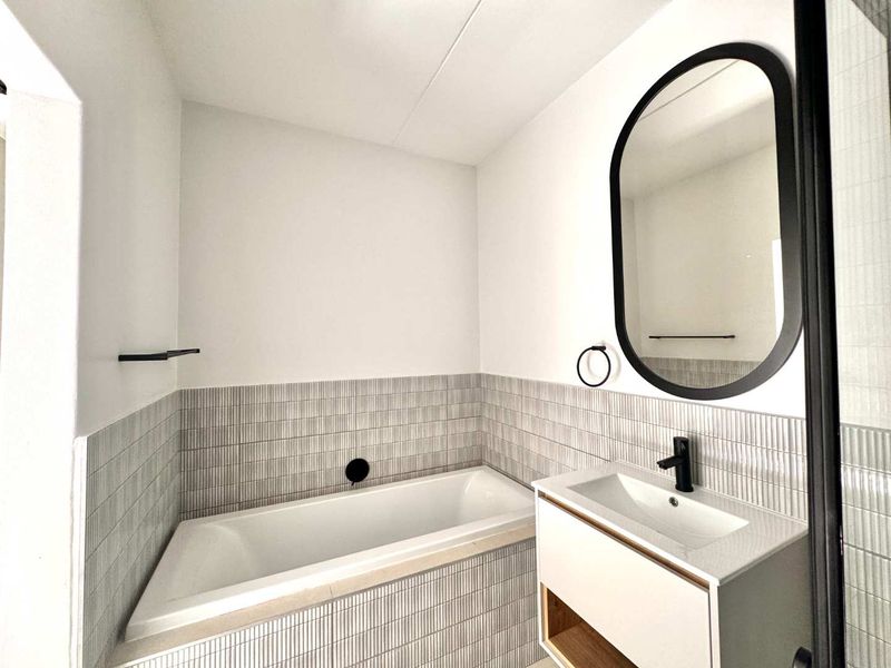 Modern bathroom featuring a built-in bathtub, contemporary vanity with basin, and stylish tiled finishes with matte black fixtures.