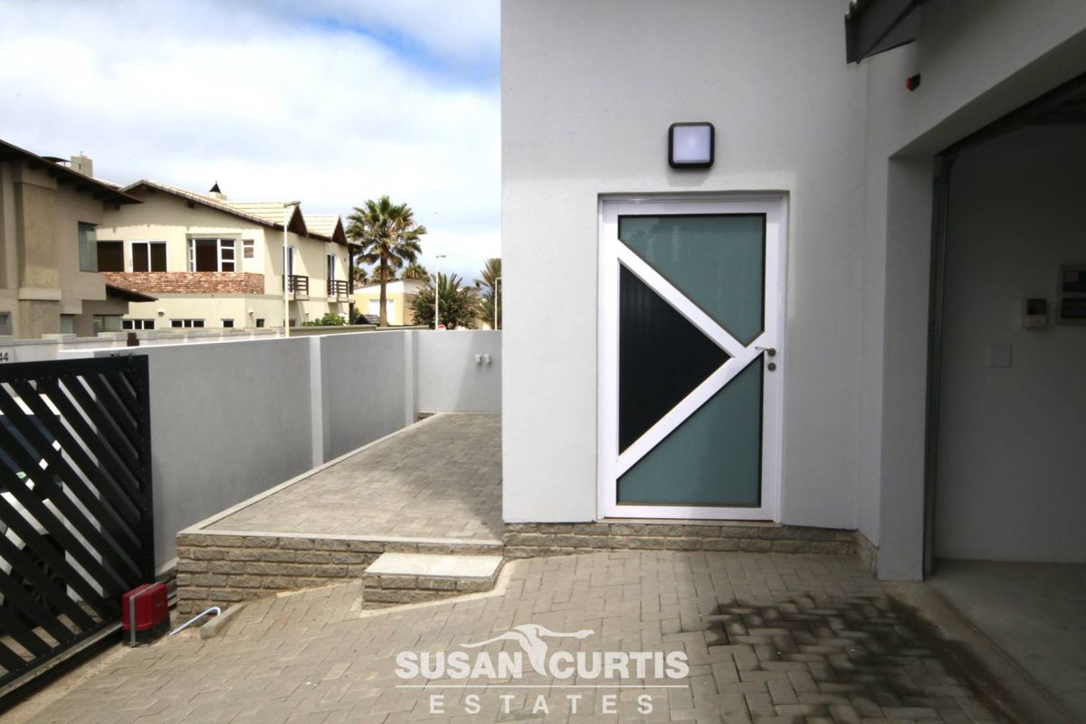 A paved exterior side area featuring a modern glass-panelled door, external wall lighting, and a perimeter boundary wall.