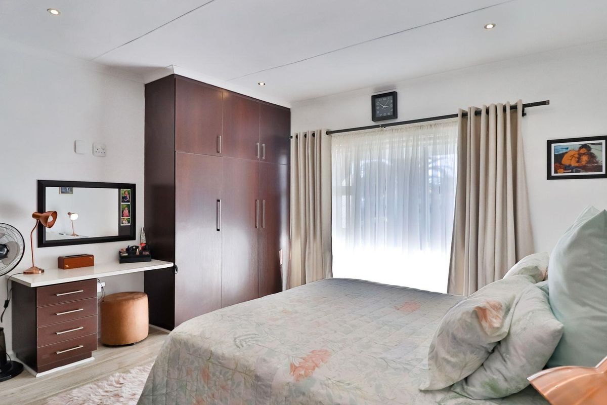 A well-maintained bedroom featuring built-in dark wood cabinetry, a dedicated vanity area, and large windows with curtain tracks.