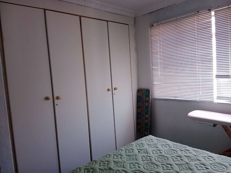A bedroom featuring built-in cupboards and venetian blinds, offering functional storage and natural light control.