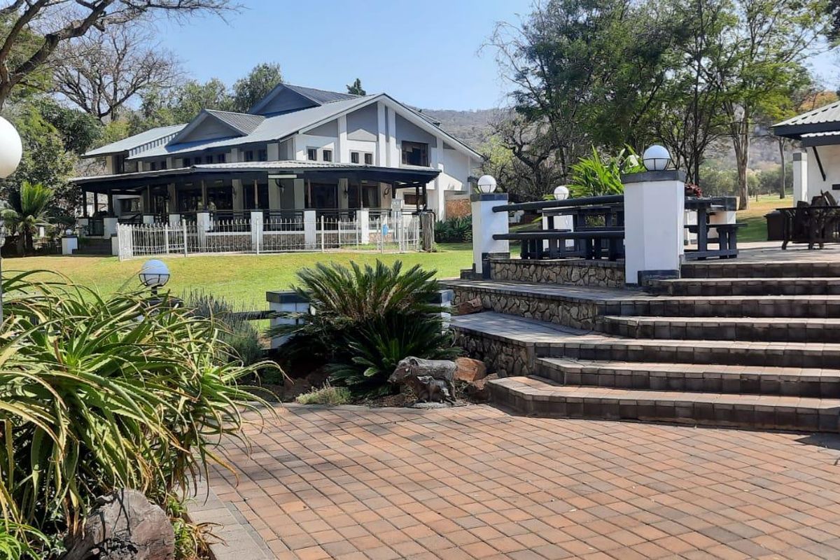 A spacious rear patio area featuring paved flooring, stone-clad steps, and well-maintained garden landscaping, overlooking the main farmhouse structure.