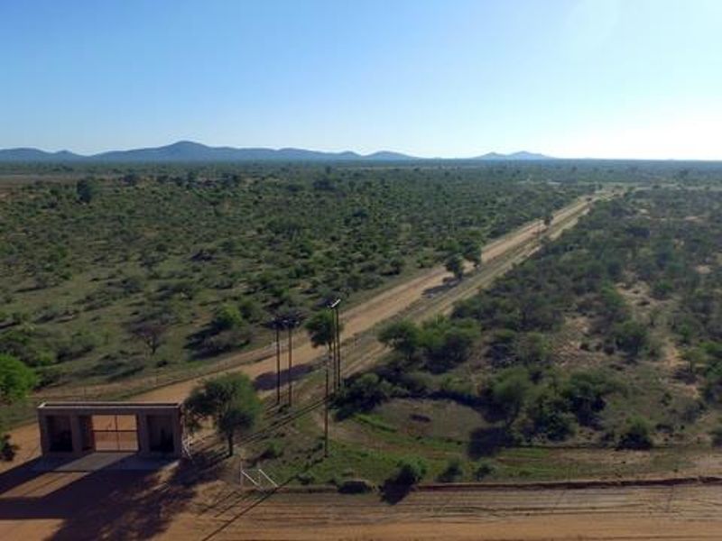 Aerial view of a rural farm property featuring a gated entrance, perimeter fencing, and expansive natural landscape with a dirt access road.
