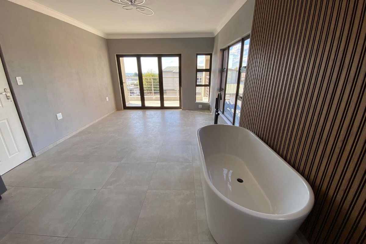 Spacious bedroom featuring a modern freestanding bathtub, tiled flooring, decorative wood-slat wall paneling, and large glass doors leading to a balcony.