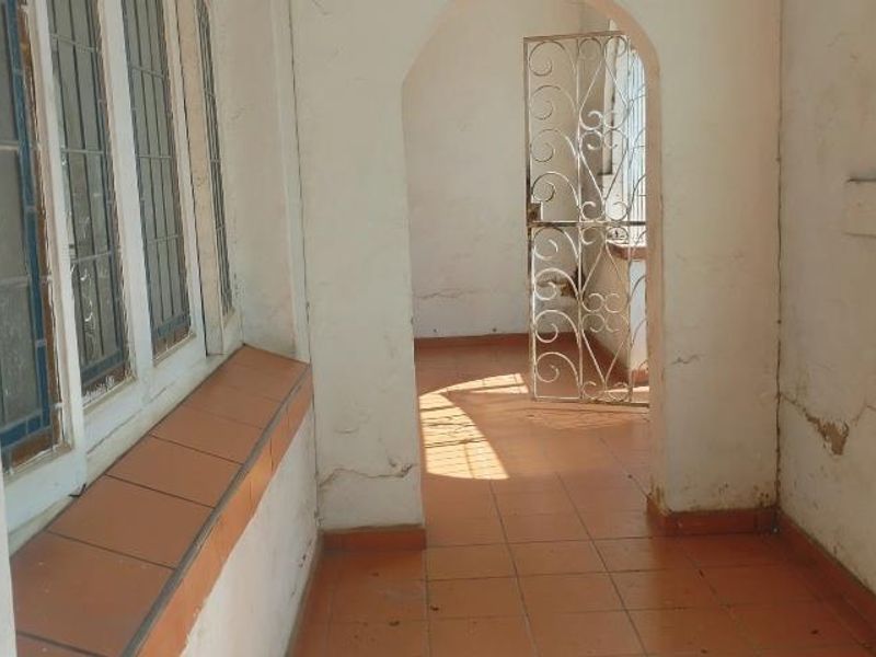 A covered patio area featuring tiled flooring, security gates, and leaded glass windows, currently showing signs of wear and requiring maintenance.