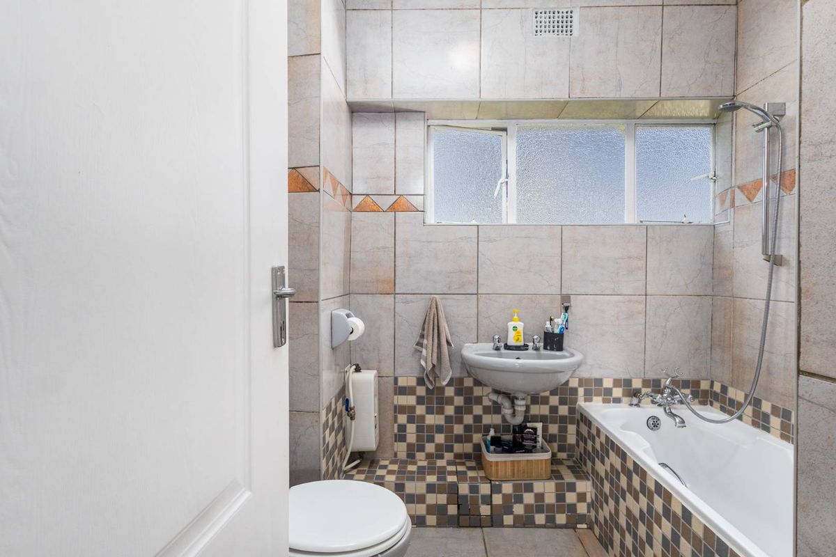 A functional bathroom featuring a bathtub with a handheld shower attachment, a wall-mounted basin, and a toilet, finished with neutral wall and mosaic floor tiles.