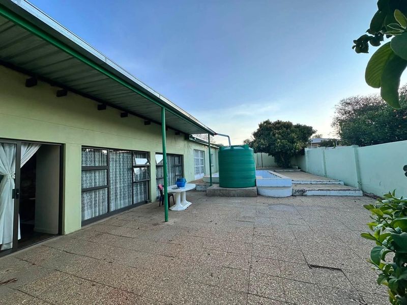 Rear exterior view featuring a paved patio area, covered veranda, and a large water storage tank against a boundary wall.