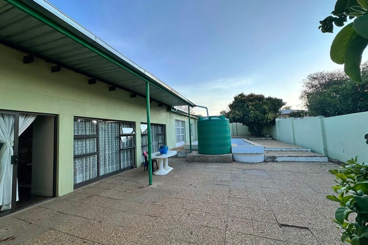 Rear exterior view featuring a paved patio area, covered veranda, and a large water storage tank against a boundary wall.