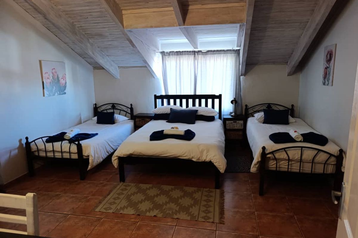 Spacious bedroom featuring a vaulted ceiling with exposed timber beams and terracotta floor tiles, comfortably accommodating multiple beds.