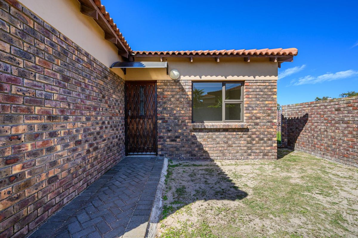 Rear exterior view of the townhouse featuring face-brick walls, a paved walkway, a security gate, and a small private garden area.