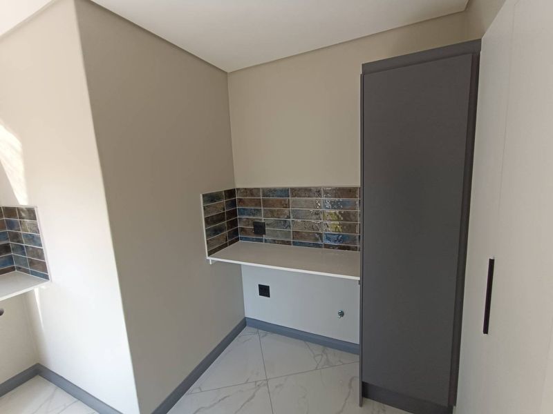 A clean, modern laundry area featuring built-in cabinetry, a stone-look countertop, and decorative tiled splashback with dedicated plumbing connections.