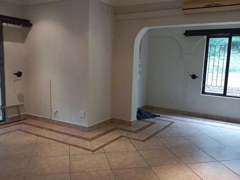 An empty, open-plan living area featuring tiled floors with decorative borders, recessed lighting, and an arched transition to an adjacent space.