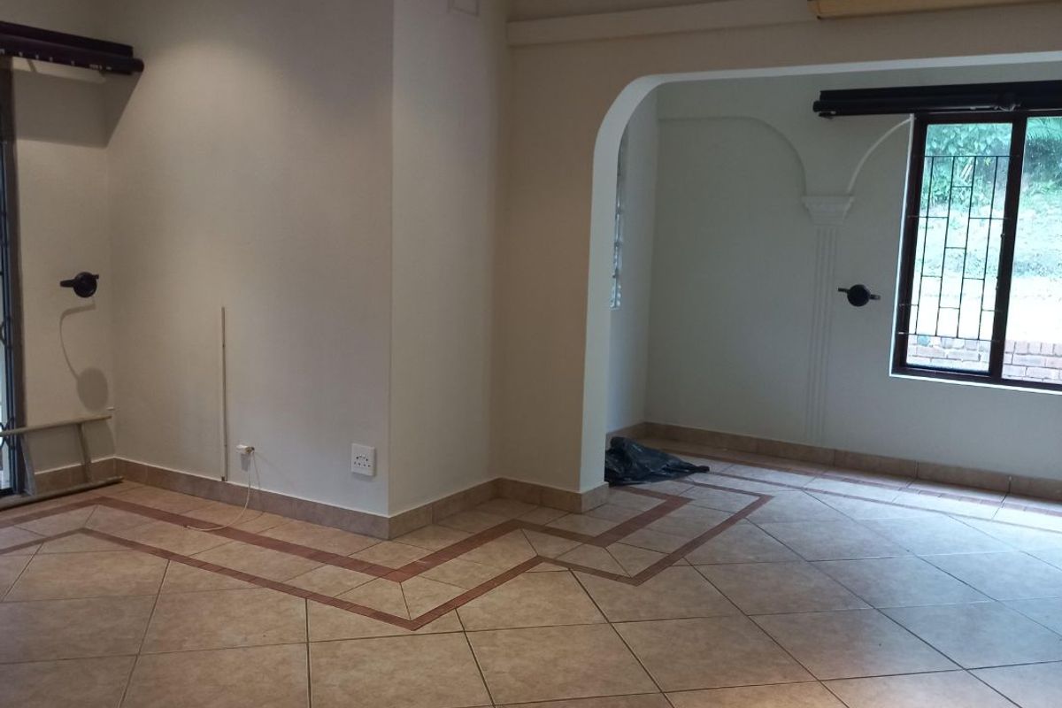An empty, open-plan living area featuring tiled floors with decorative borders, recessed lighting, and an arched transition to an adjacent space.