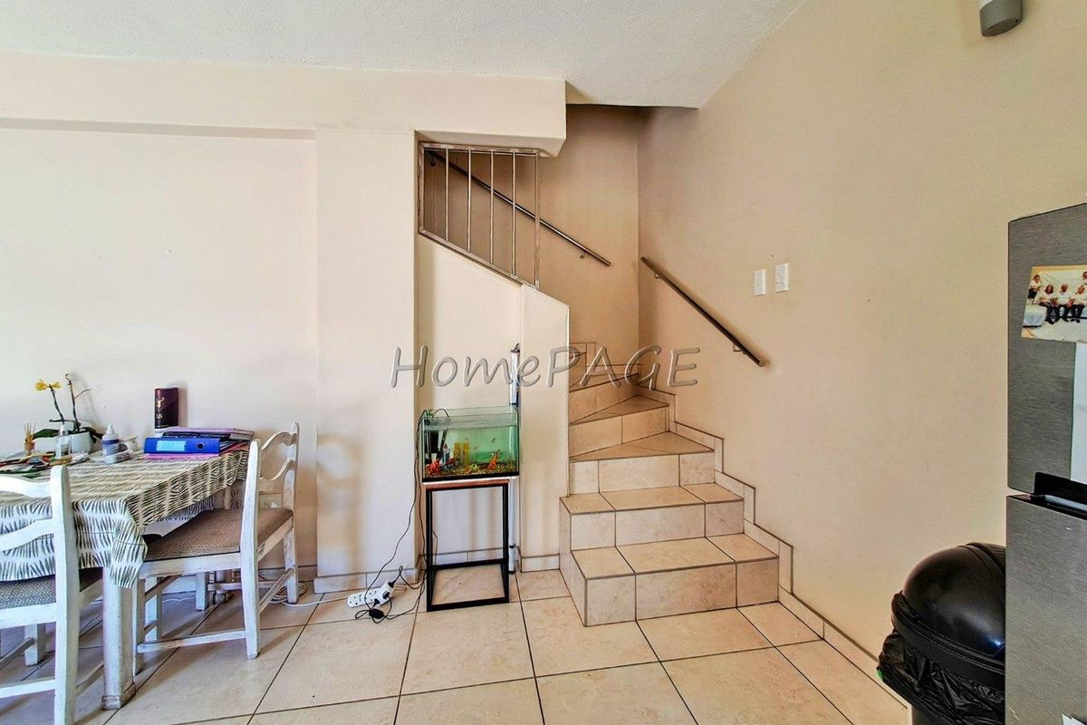Interior view of a living area featuring a tiled staircase with a metal handrail and ceramic floor tiling throughout.