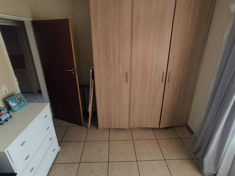 A bedroom featuring light wood-finish built-in wardrobes and neutral tiled flooring, providing functional storage space.