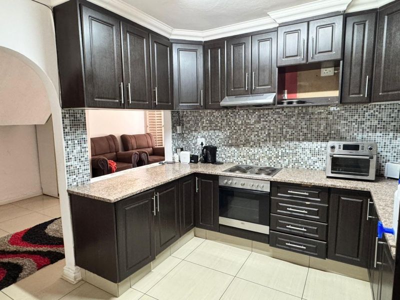 A functional kitchen featuring dark wood cabinetry, granite countertops, and a mosaic tile backsplash, with an open-plan layout connecting to the living area.