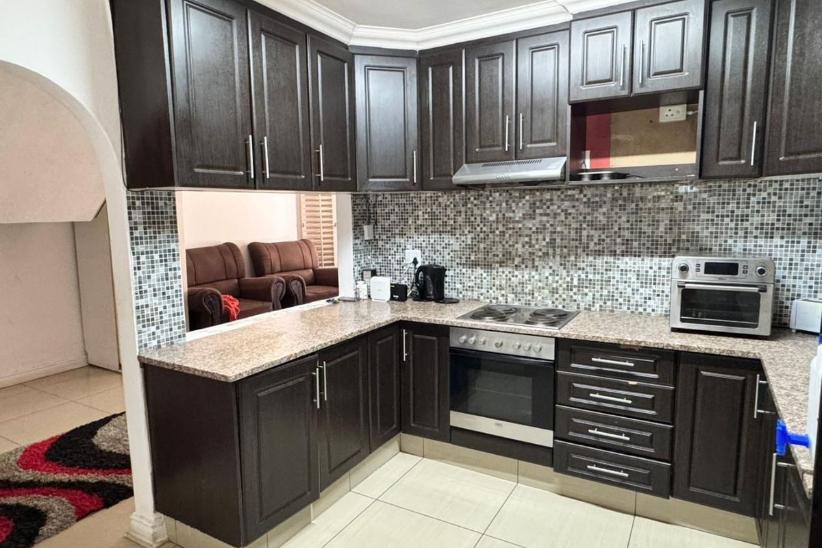 A functional kitchen featuring dark wood cabinetry, granite countertops, and a mosaic tile backsplash, with an open-plan layout connecting to the living area.
