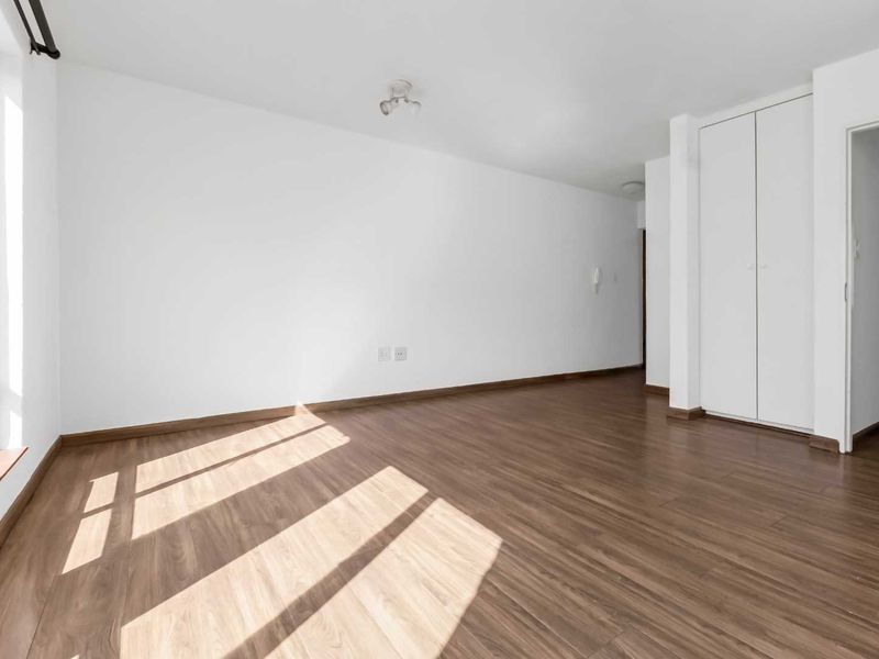 A bright, empty bedroom featuring modern laminate flooring, a built-in wardrobe, and large timber-framed windows allowing for ample natural light.