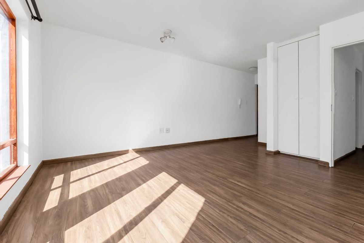 A bright, empty bedroom featuring modern laminate flooring, a built-in wardrobe, and large timber-framed windows allowing for ample natural light.