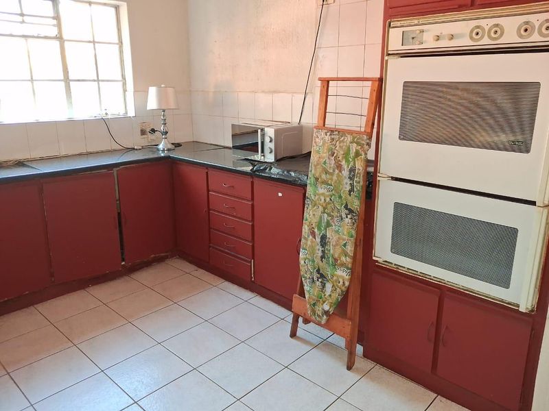A dated kitchen featuring red cabinetry, a double wall oven, tiled flooring, and a tiled backsplash, offering potential for a modern renovation.